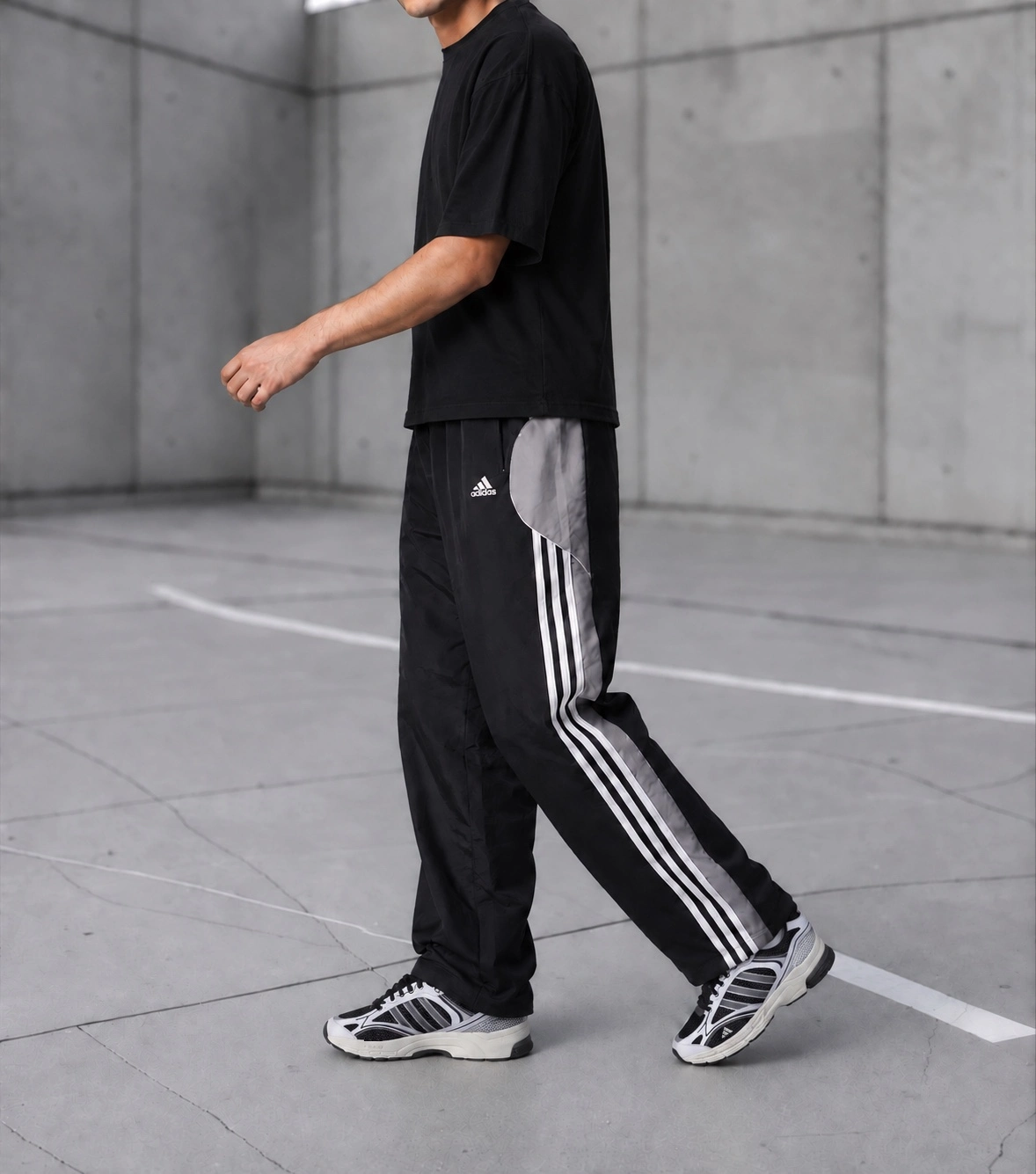 Schwarze Vintage-Trackpants mit grauen Einsätzen, getragen auf einem Betonplatz